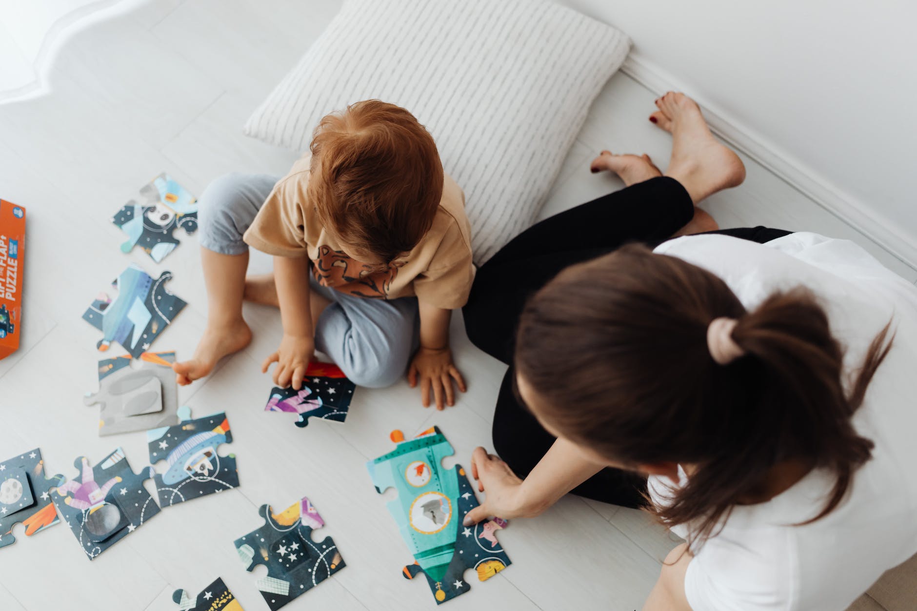 overhead shot of a kid in a brown shirt solving a jigsaw puzzle