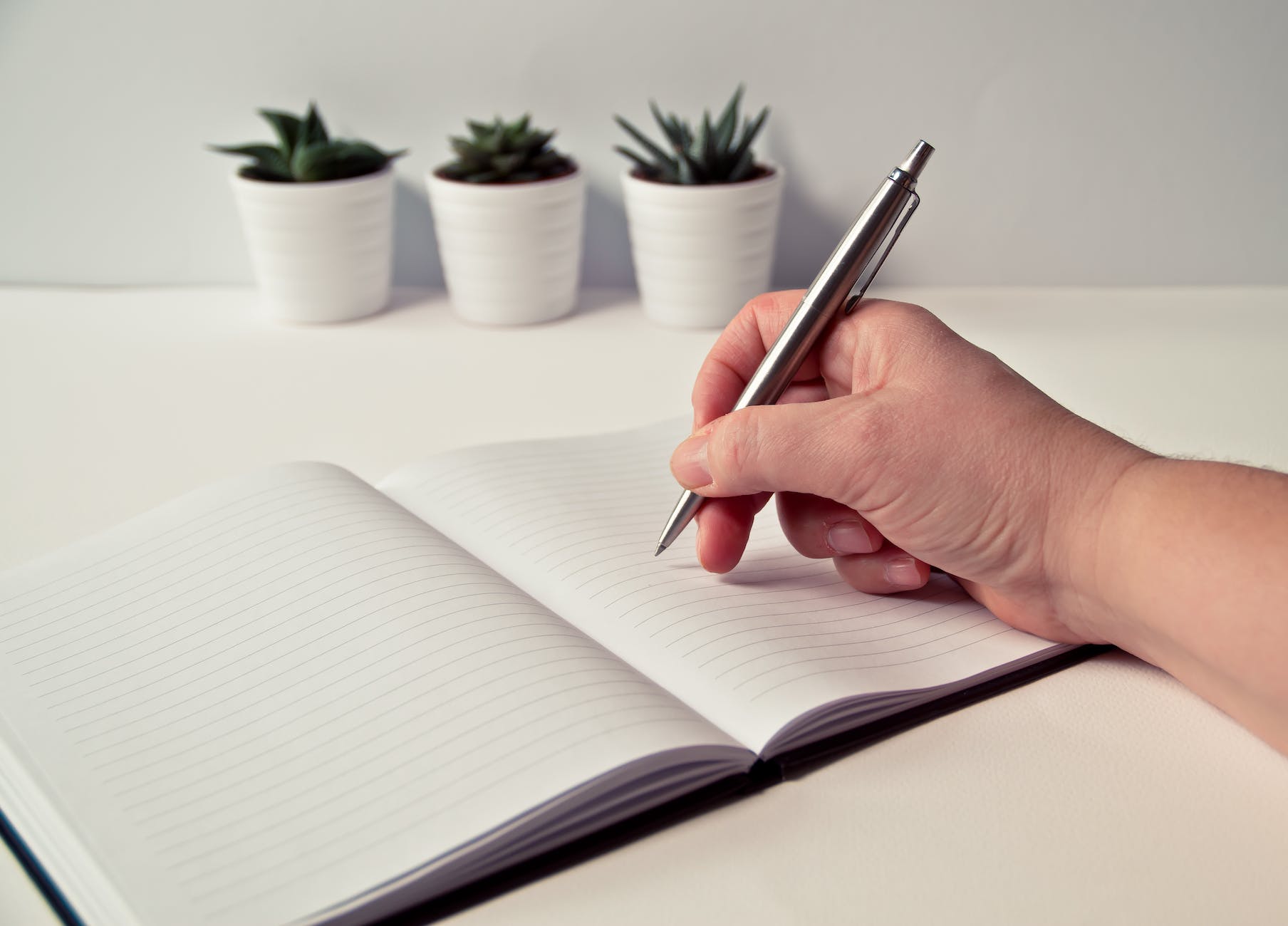 person holding silver retractable pen in white ruled book